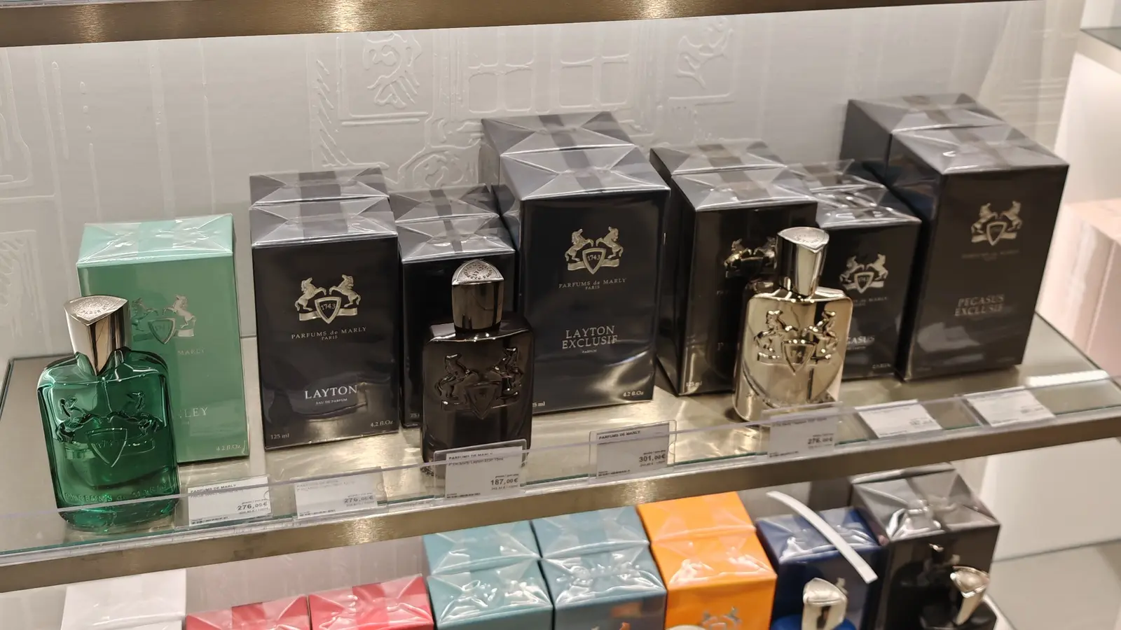 Glass shelves of Parfums de Marly bottles beside their black and white boxes in a perfumery