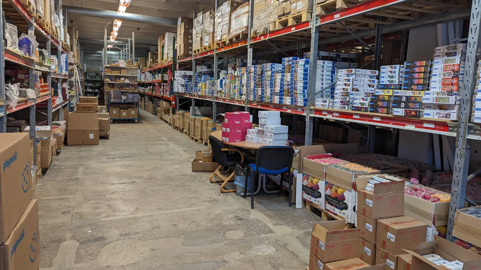 Long warehouse aisle with steel shelving stacked with cartons and boxed stock